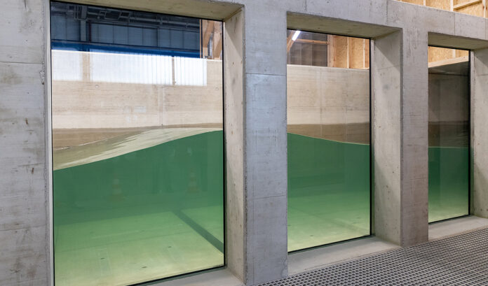 Durch ein großes Unterwasserfenster können die Forscherinnen und Forscher wie bei einem Aquarium in den neuen Wellenkanal schauen. Bild: Kristina Rottig/TU Braunschweig